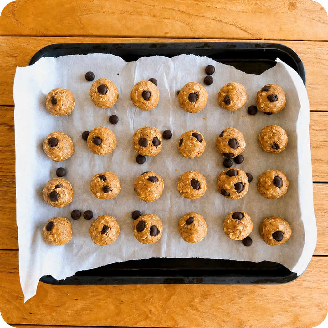 Two dozen oat and peanut butter energy balls studded with chocolate chips, cooling on a parchment-lined tray