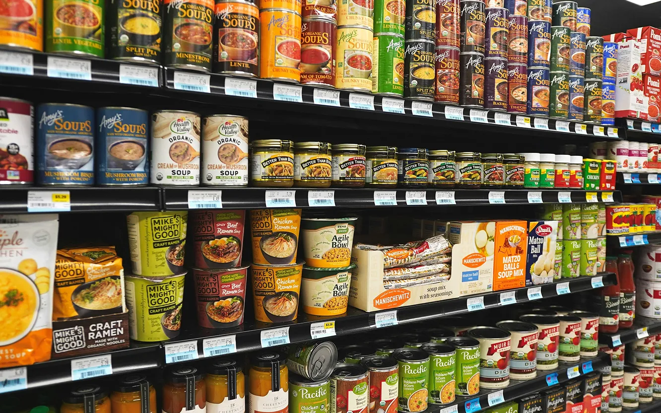 Shelves of canned soups, packaged ramen and jars in a grocery aisle