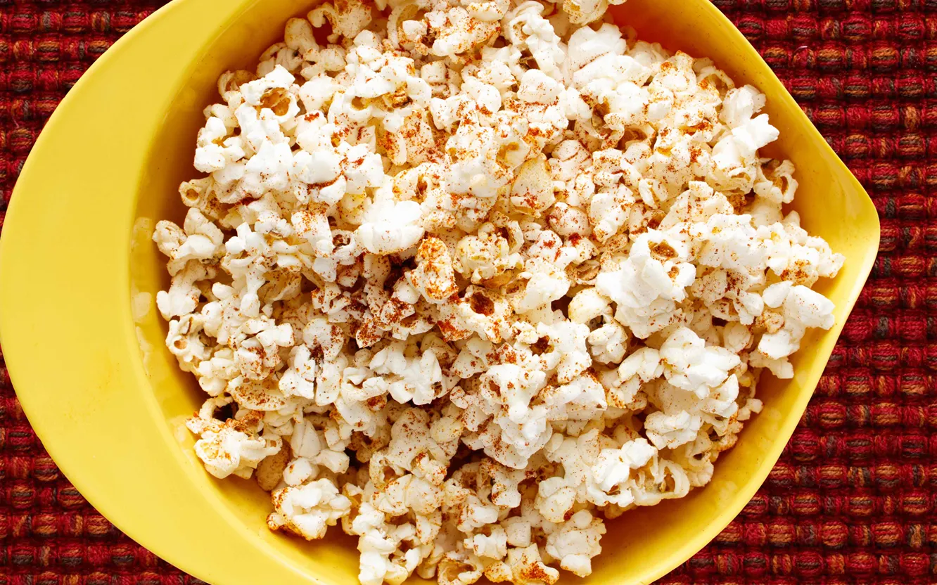 Chili popcorn in yellow bowl on red tablecloth.