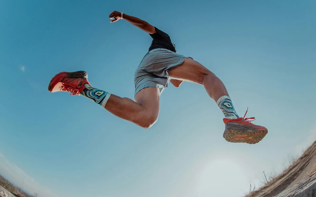 A runner leaping through the air against a blue sky, photographed from below