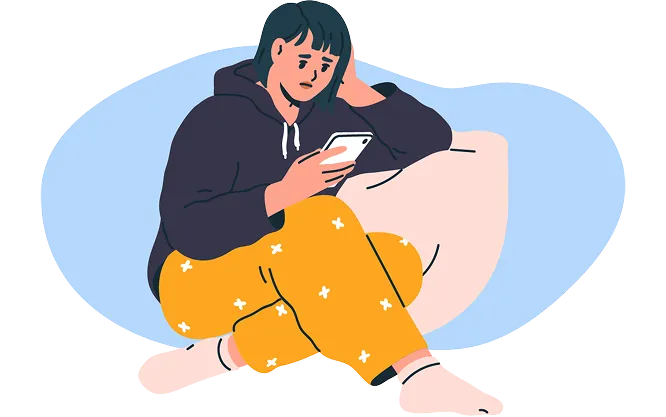 A person sitting on the floor in a hoodie, looking at their phone